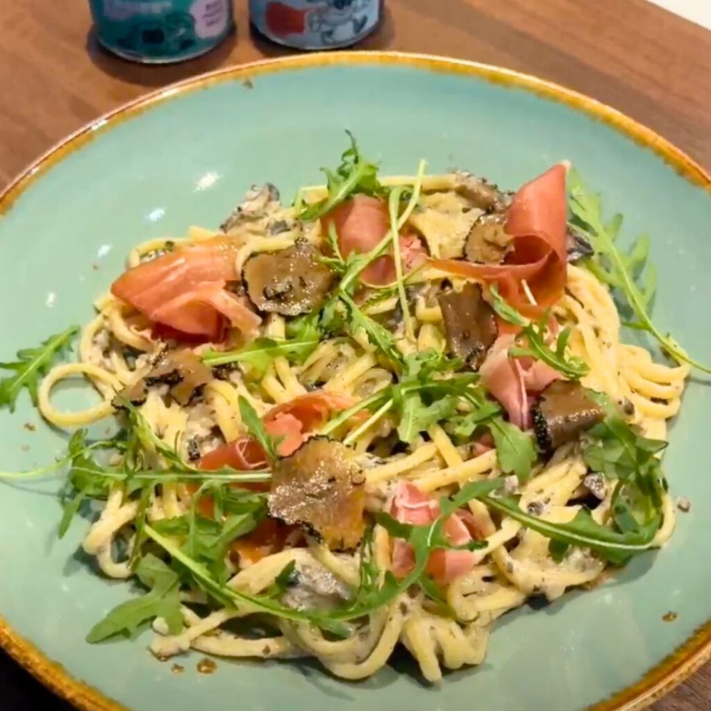 Spaghetti met romige champignonsaus, parmaham, truffelschijfjes en verse rucola op een groen bord